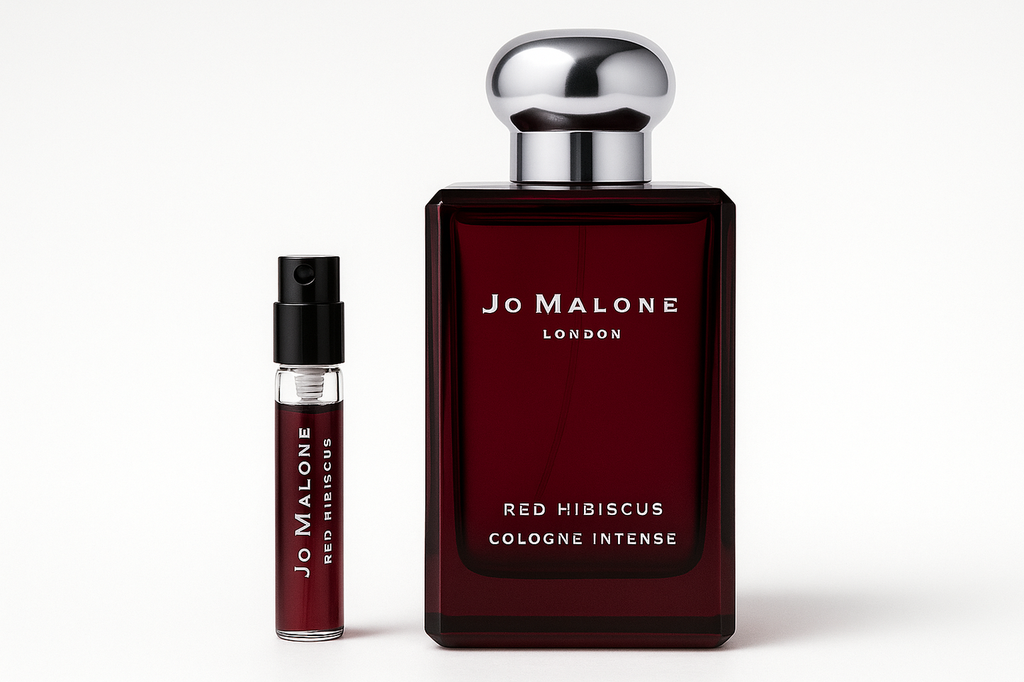 Jo Malone Red Hibiscus Cologne Intense 2ml 샘플이 진한 빨간색 병에 흰색 글씨가 적힌 Jo Malone Red Hibiscus Cologne Intense 100ml 향수병 옆에 서 있습니다.