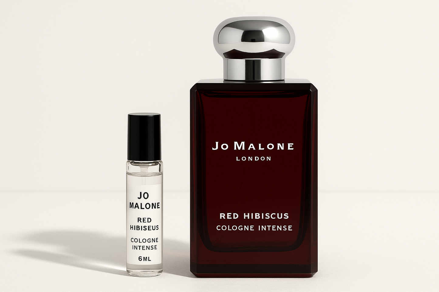 Jo Malone Red Hibiscus Cologne Intense 6ml 샘플이 진한 빨간색 병에 흰색 글씨가 적힌 Jo Malone Red Hibiscus Cologne Intense 100ml 향수병 옆에 서 있습니다.